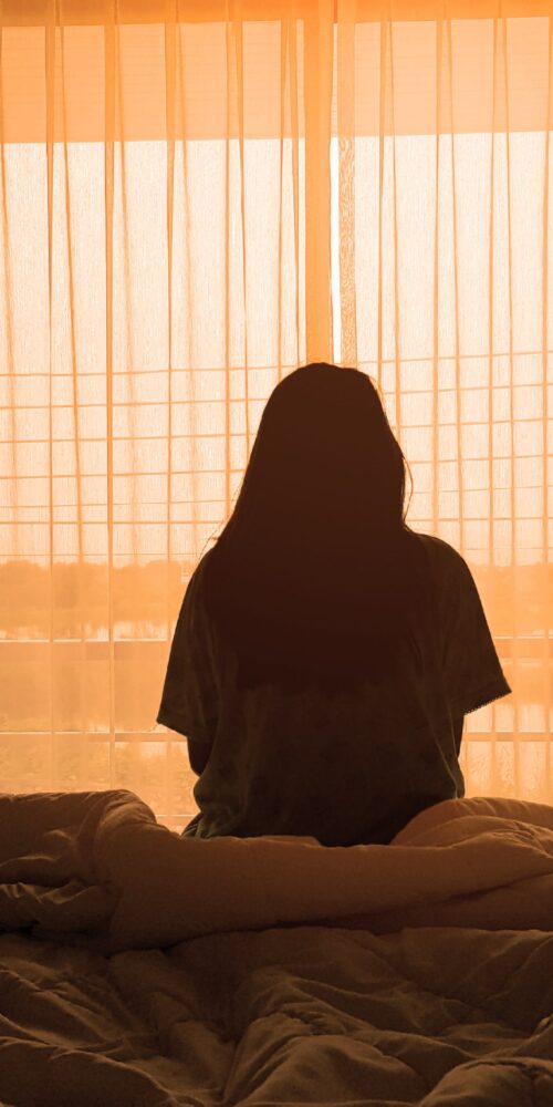 Woman sitting on bed with little sunlight.